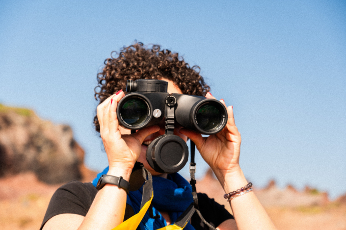 A woman with short curly hairs is looking through binoculars