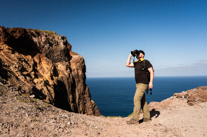 Explorer with binoculars on a rocky cliff by the sea with blue sky