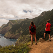 A couple both in red shirts are hiking the stunning landscapes of the shore of Madeira island