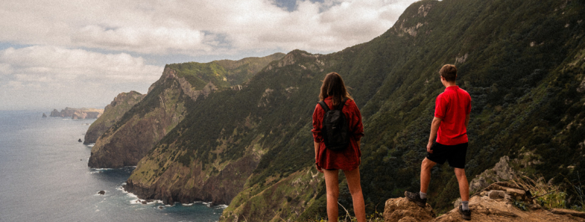 A couple, both in red shirts, standing on a cliff looking at the northern coast of Madeira island