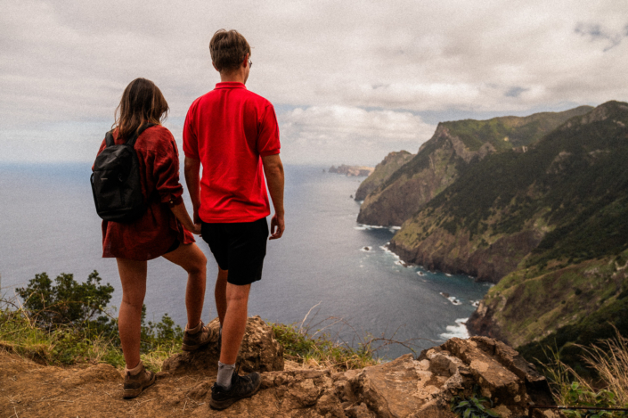A couple in red shirts are standing on a cliff by the sea on Madeira island, landscape format