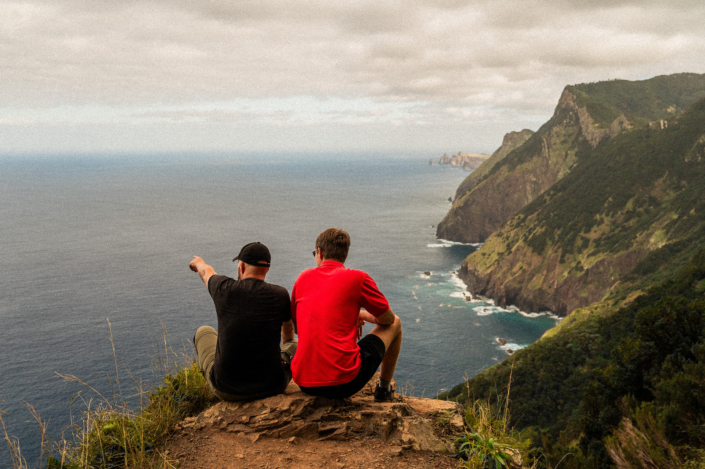 Two male nomads are sitting on a cliff at the shore of Madeira island