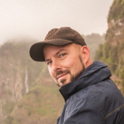 A guy with a hat sitting in front of a waterfall